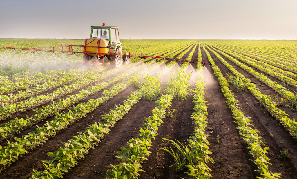 Tractor spraying pesticides on soy field because they understand hobby farms vs. commercial farming