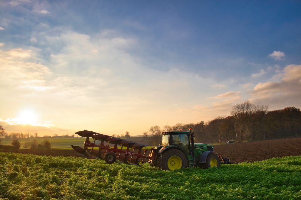 A tractor works on a beautiful farm as the sun sets on the horizon