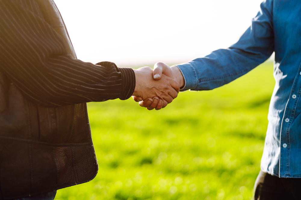 Handshake between two men in front of a wheat field purchased with an agriculture land loan. The concept of the agricultural business.